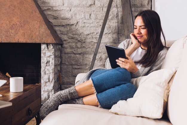 Moderne Frau, die auf dem Sofa unter Verwendung einer Tablette sitzt