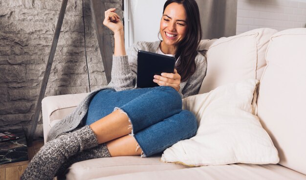 Moderne Frau, die auf dem Sofa unter Verwendung einer Tablette sitzt