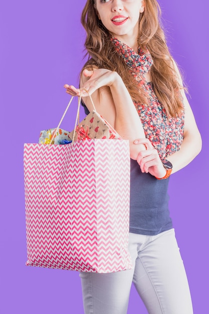 Moderne Frau, die Einkaufstasche voll von eingewickeltem Geschenk hält