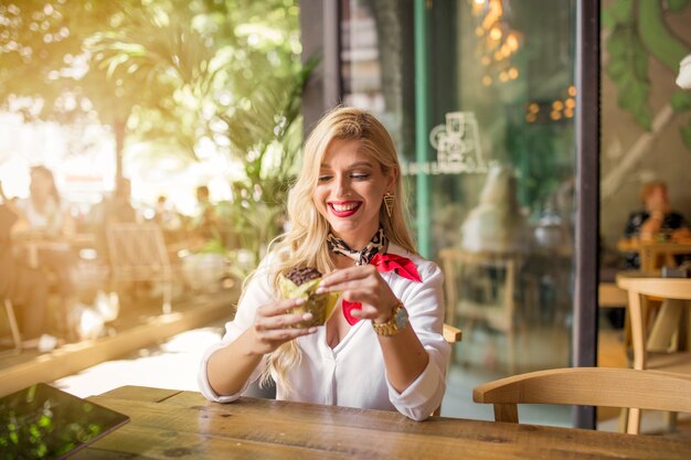 Moderne junge Frau, die im caf� isst Muffin sitzt