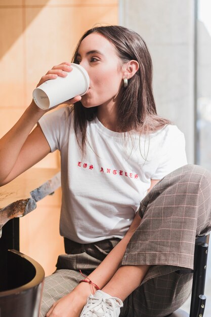 Moderne junge Frau, die im Café trinkt den Kaffee sitzt