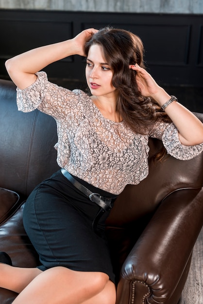 Moderne junge Frau mit den Händen in ihrem Kopf, der auf braunem Sofa sitzt