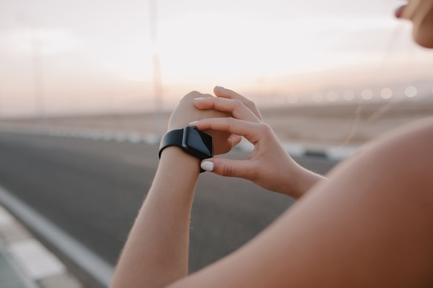 Moderne Uhr des Nahaufnahmeporträts auf Händen der Sportlerin auf Straße im sonnigen Morgen. Training, Training, wahre Emotionen, gesunder Lebensstil, fleißig