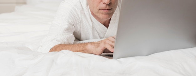 Moderner älterer Mann, der einen Laptop im Bett verwendet