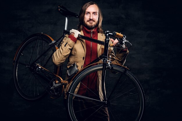 Moderner bärtiger Hipster im roten Pullover hält sein Fahrrad, während er für Fotografen posiert.