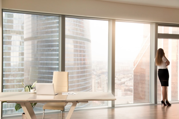 Kostenloses Foto moderner büroinnenraum mit dem weiblichen schattenbild, das am in voller länge fenster steht