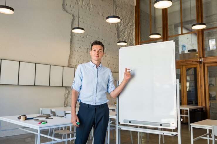 Kostenlose Foto moderner junger hübscher lächelnder mann, der an leerer weißer tafel mit markierung steht,