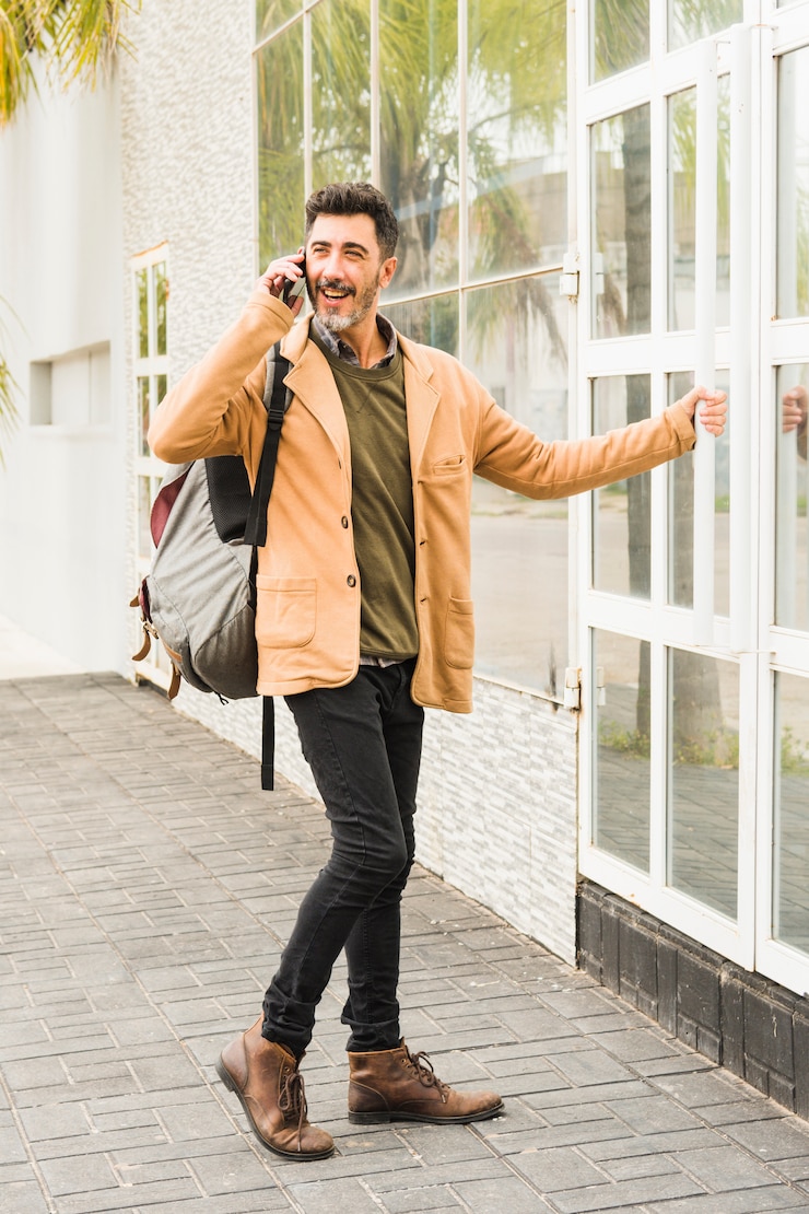 Kostenlose Foto moderner lächelnder mann mit seinem rucksack sprechend am handy beim öffnen der glastür