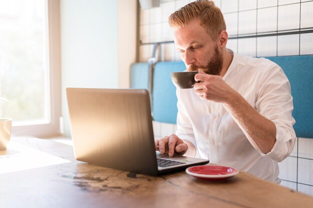 Moderner Mann, der an seinem Laptop beim Kaffeetrinken arbeitet