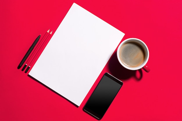 Moderner roter Schreibtisch mit Smartphone und Tasse Kaffee.