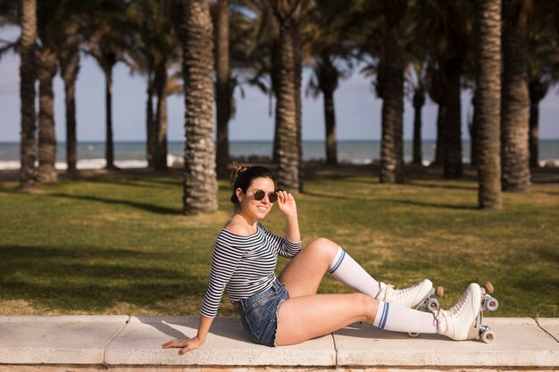 Moderner tragender Rollschuh der jungen Frau, der vor Strand sitzt