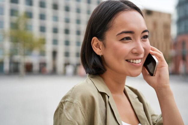 Modernes junges asiatisches Mädchen, das auf dem Handy spricht, benutzt das Telefon auf der Stadtstraße Frau lächelt während des Anrufs