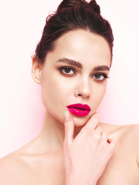 Modeschönheitsporträt einer jungen brünetten Frau mit stilvollem Make-up am Abend und perfekt sauberer Haut Sexy Model mit Haaren in einem Brötchen posiert im Studio in der Nähe einer weißen Wand mit rosafarbenen, hellen, natürlichen Lippen