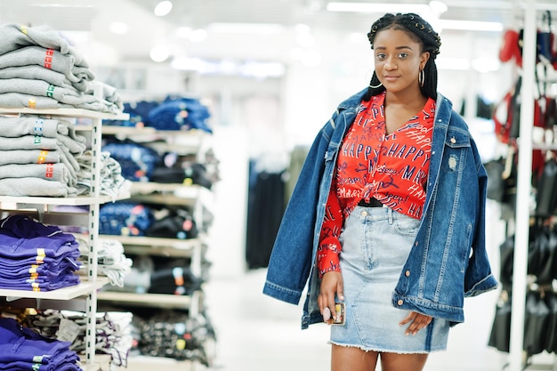 Modische afrikanisch-amerikanische Frau in rotem Hemd und Jeansrock mit Jacke posiert im Bekleidungsgeschäft Es ist Zeit zum Einkaufen