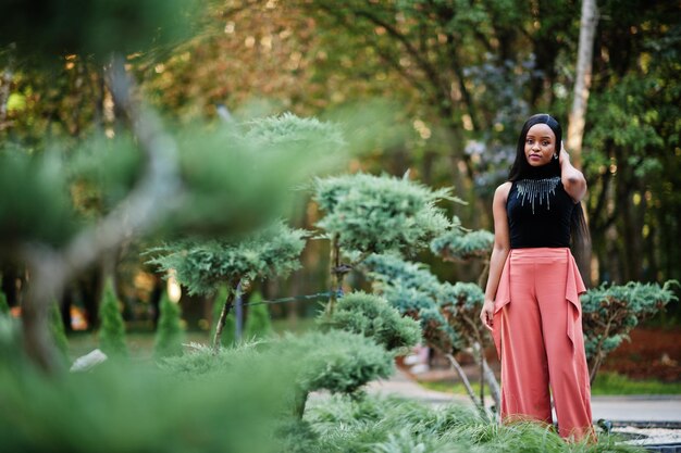 Modische Afroamerikanerin in Pfirsichhosen und schwarzer Bluse posiert im Freien