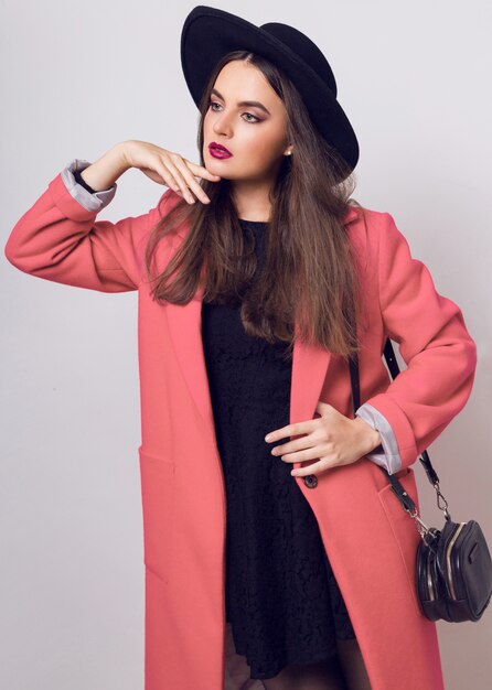 Modische Frau im rosa Mantel und im schwarzen Hut, der aufwirft