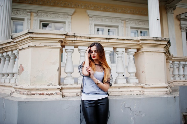 Modische Frau schaut auf weißes Hemd schwarze transparente Kleidung Lederhose posiert auf der Straße gegen altes Haus mit Fenstern und Säulen Konzept der Mode Mädchen