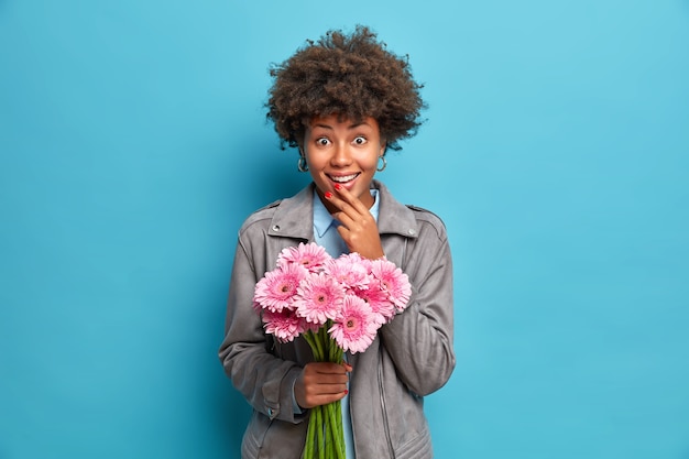 Modische junge afroamerikanische Frau erhält Blumenstrauß von rosa Gerbera-Blumen von liebendem Freund während des Datums