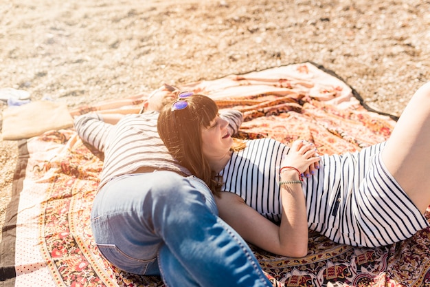 Modische junge Paare, die auf Decke am Strand liegen