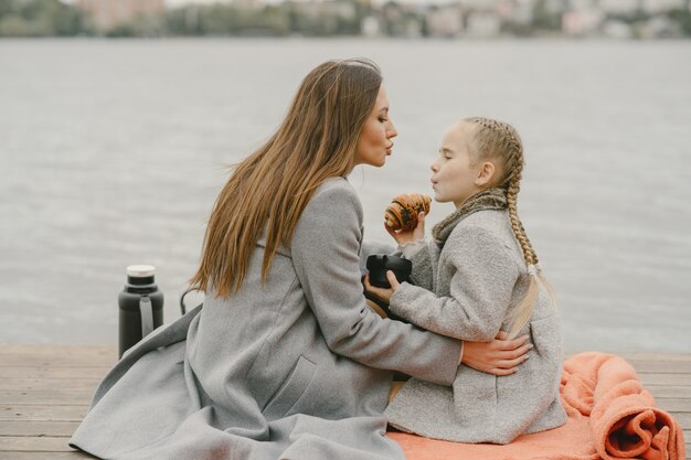 Modische Mutter mit Tochter. Leute auf einem Picknick. Frau in einem grauen Mantel. Familie am Wasser.