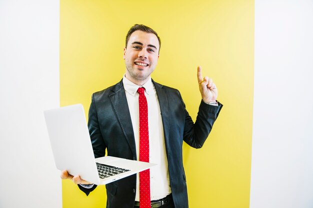 Modischer Mann mit dem Laptop, der Finger hochhält