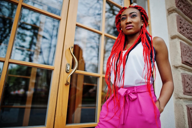 Modisches afrikanisch-amerikanisches Mädchen in rosa Hosen und roten Dreads posierte im Freien