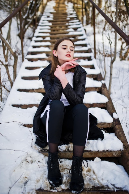 Modisches brünettes Model mit langen Beinen im langen schwarzen Mantel posierte im Freien am Wintertag