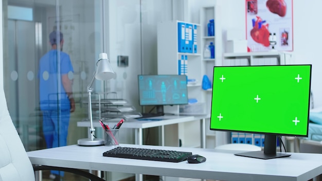 Monitor mit grünem Bildschirm im Krankenhaus, während männlicher Assistent auf Aufzug wartet. Computer mit Leerzeichen verfügbar auf Medizinspezialist im Klinikschrank.