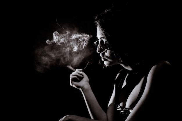 Monochromes Porträt des jungen Mädchens, das mit großem Dekolleté und in Brillen raucht