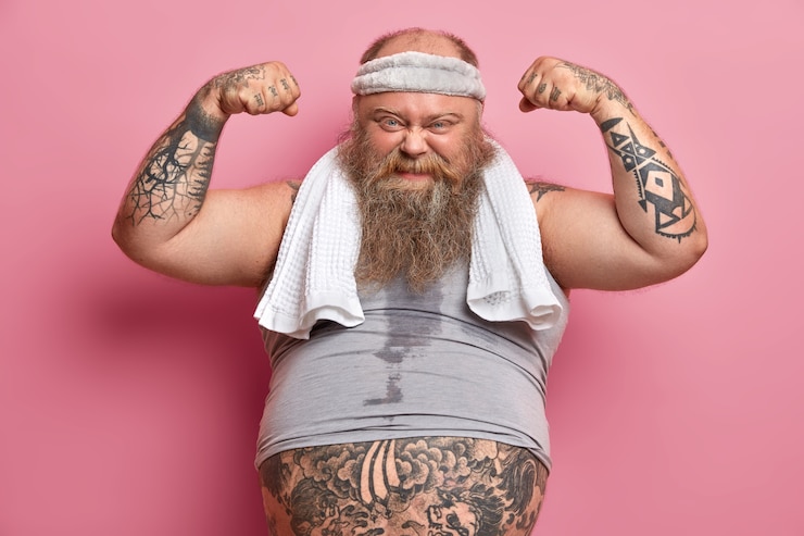 Kostenlose Foto motivierter übergewichtiger bärtiger mann hebt die arme, zeigt muskeln nach dem training, will stark sein und bizeps haben, führt einen gesunden lebensstil, hat ein fitnessprogramm für gewichtsverlust, vertrauen in sich.