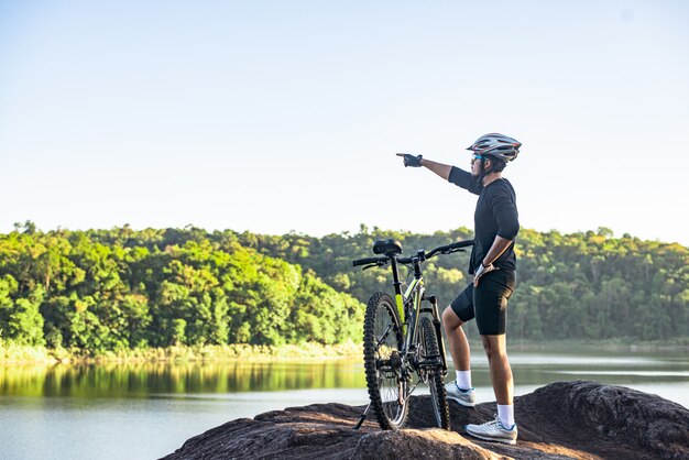 Mountainbiker stehen mit dem Fahrrad oben auf dem Berg und zeigen mit dem Finger nach vorne.