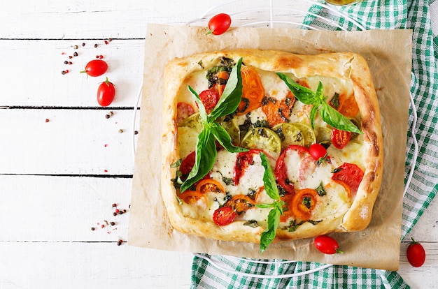 Mozzarella, Tomaten, wohlschmeckende Torte des Basilikums auf einem weißen Holztisch. Leckeres Essen, Vorspeise im mediterranen Stil. Ansicht von oben. Flach liegen