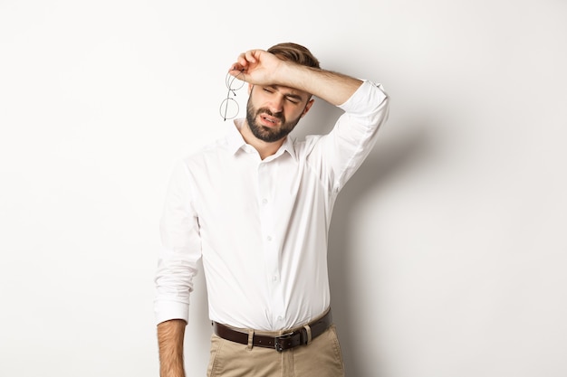 Müde Büroangestellte nehmen die Brille ab, wischen sich mit dem Arm den Schweiß von der Stirn und stehen erschöpft da