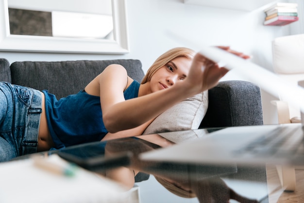 Müde Frau, die auf Sofa liegt und Laptop zu Hause schließt