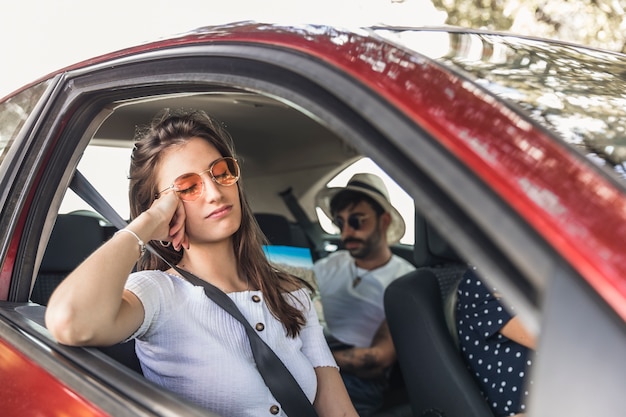 Müde junge Frau, die im Auto mit ihren Freunden schläft