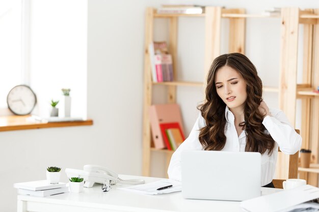 Müde junge Geschäftsfrau, die unter langer Zeit leidet, die am Computertisch im Büro sitzt