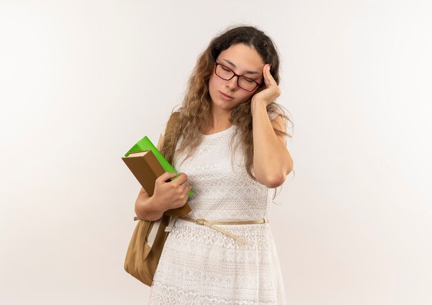 Müde junge hübsche Schulmädchen, die Brille und Rückentasche hält Bücher hält Hand auf Kopf mit geschlossenen Augen lokalisiert auf Hintergrund mit Kopienraum