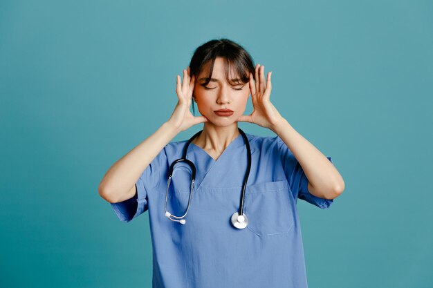 Müde junge Ärztin mit einheitlichem Fith-Stethoskop isoliert auf blauem Hintergrund
