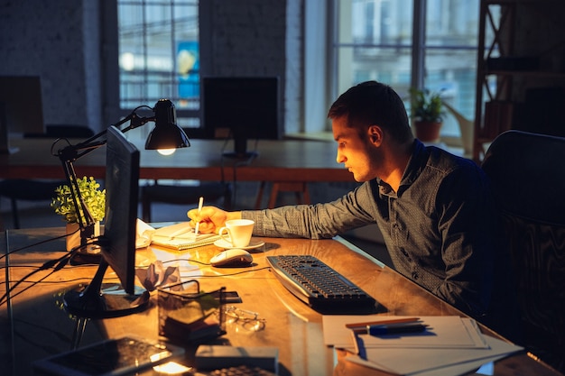 Müde. Mann, der allein im Büro arbeitet und bis spät in die Nacht bleibt.