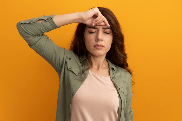 Müde mit geschlossenen Augen junges schönes Mädchen, das olivgrünes T-Shirt trägt Hand auf Stirn lokalisiert auf gelber Wand