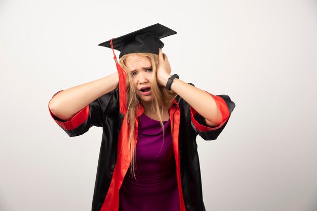 Müde Studentenfrau, die ihre Ohren auf Weiß bedeckt.