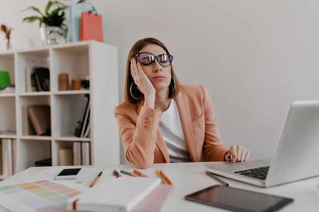 Müder Arbeiter, der Brille trägt, die am Arbeitsplatz einschlafen. Snapportrait der Dame in der Jacke im weißen Büro.