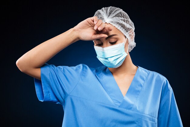 Müder Arzt in medizinischer Maske und Kappe wischen Schweiß isoliert