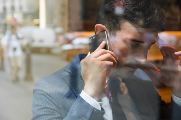 Müder Geschäftsmann, der am Telefon im Café spricht