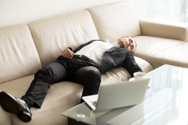 Müder Geschäftsmann, der auf Sofa im Büro schläft