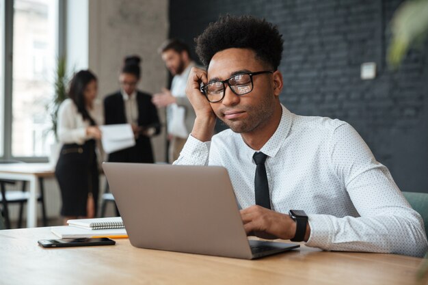 Müder junger afrikanischer Geschäftsmann unter Verwendung der Laptop-Computers