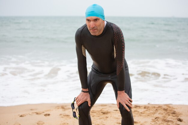 Müder männlicher Schwimmer, der am Strand steht