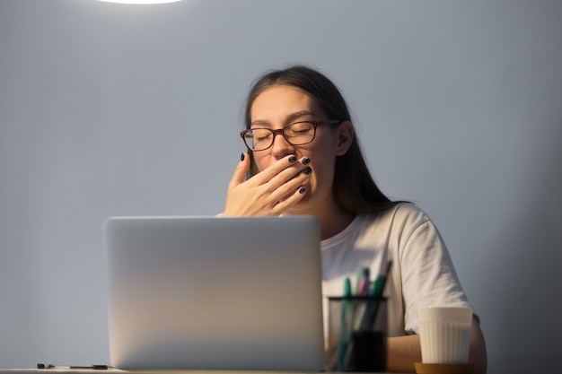 Müder Sekretär, der spät nachts an Laptop-Computer arbeiten gähnt.