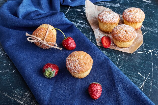 Muffins mit Erdbeeren auf blauer Oberfläche.