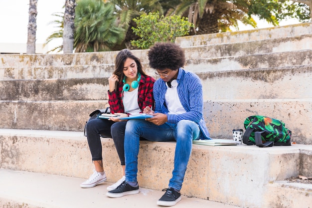 Multi ethnische junge Paare, die auf dem Treppenhaus zusammen studieren im Park sitzen